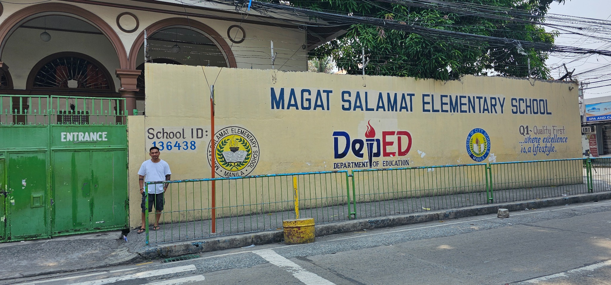 Romeo standing beside the entrance of Magat Salamat Elementary School during his 2024 return visit.
